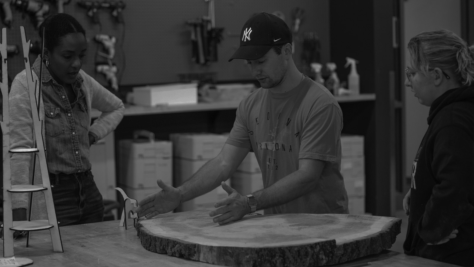 a man measuring a piece of wood with his hands while two women watch