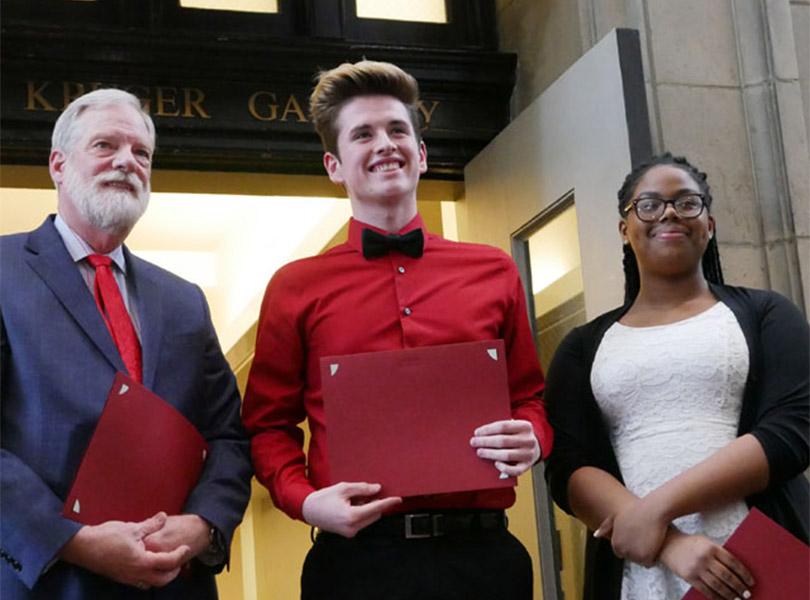 three individuals standing together holding red plaques and smiling