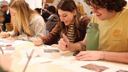 students sketching on paper while looking at reference photos