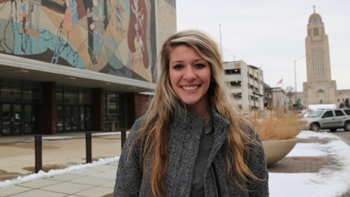 Woman outdoors near colorful mural and tall building, winter setting with snow on the ground.
