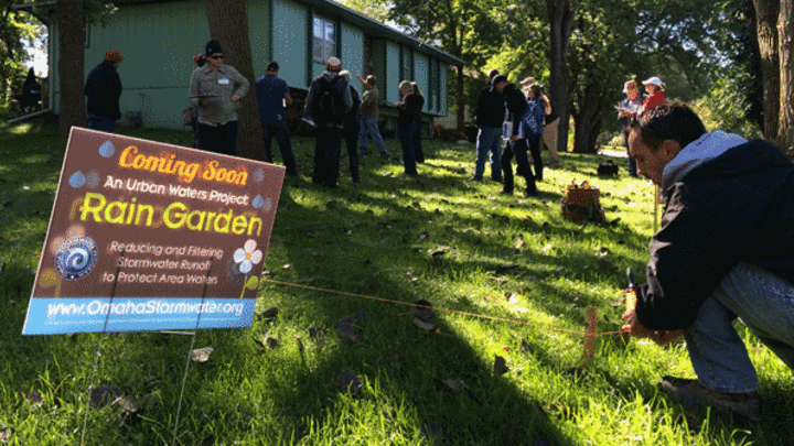 a sign stating a rainwater garden is coming soon with people in the background