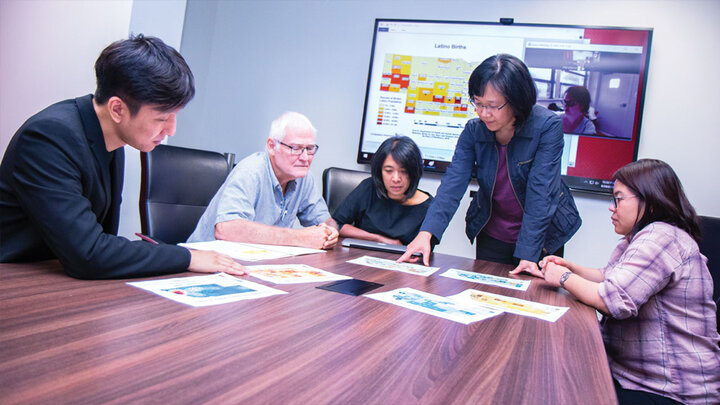 Faculty pointing at a maps of nebraska in a conference room