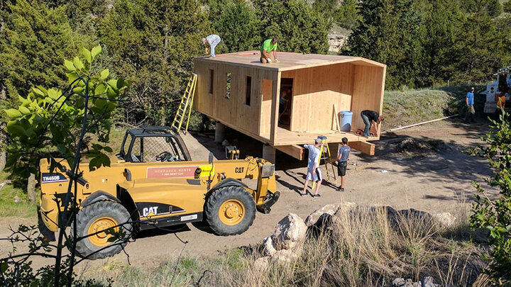 a large forklift holding up a small wooden building while students work on it