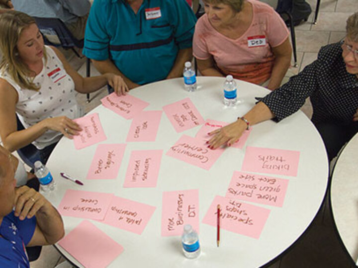 a group sat around a circular table looking at pink cards with writing