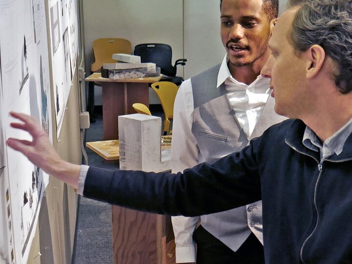 two professors talking to each other and pointing at a whiteboard