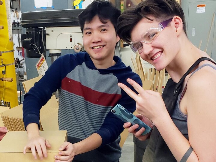 two students smiling at the camera while working on a project