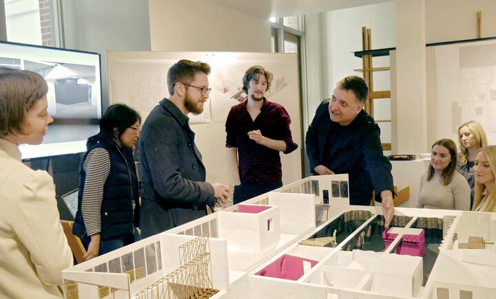 students and faculty pointing at and talking about a miniature construction of a building