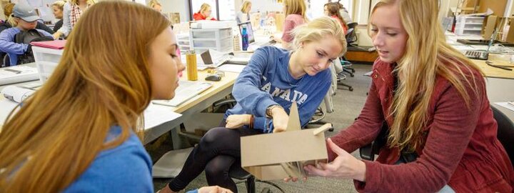 Students holding up design project while discussing it